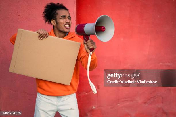 a male protestor using a megaphone and holding a blank placard - chanten stockfoto's en -beelden