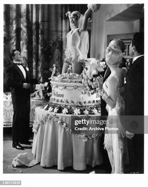 Gene Kelly watching Debbie Reynolds pop out of birthday cake in a scene from the film 'Singin' In The Rain', 1952.