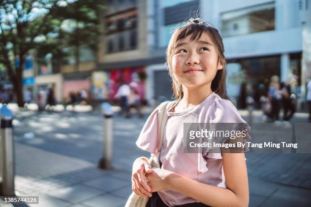 lovely cheerful girl looking up to sky while walking in downtown city street during a sunny day - only kids at sky stockfoto's en -beelden