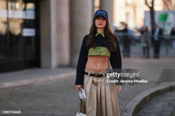 Fashion Week guest seen wearing a navy blue cap with white embroidered logo from Miu Miu, a green cropped shirt from Miu Miu, a navy blue wool...