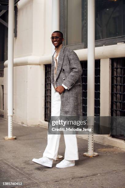 Creative and model Alioune Fall wears a long gray houndstooth coat, white top, white pants, and white Nike Air Force 1 sneakers at the Collina Strada...