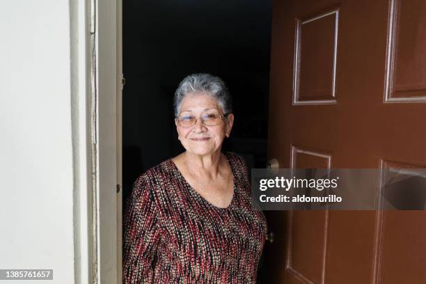 smiling senior woman standing at doorway - opening front door stock pictures, royalty-free photos & images