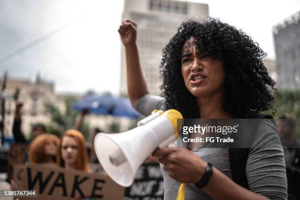 junge frau, die eine demonstration mit einem megaphon leitet - protests stock-fotos und bilder