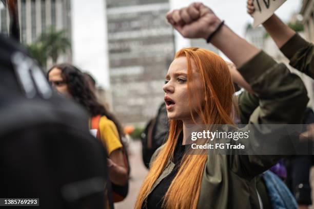 junge frau bei einer demonstration auf der straße - soziale gerechtigkeit stock-fotos und bilder