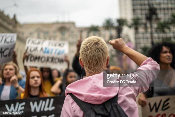 junge frau, die eine demonstration auf der straße anführt - protest stock-fotos und bilder