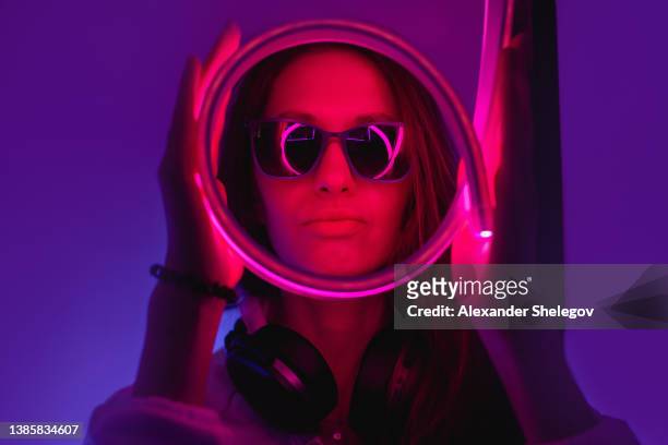 female portrait in neon light. fashion woman in purple color. vibrant background at the studio. futuristic concept. girl wear sunglasses and hoodie with bluetooth wireless headphones - cyber punk girl stock pictures, royalty-free photos & images