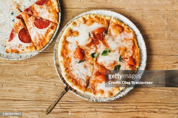 top view of delicious freshly baked sliced pepperoni and margherita pizza with ham on wooden table. mediterranean culture - cheese pizza stock-fotos und bilder