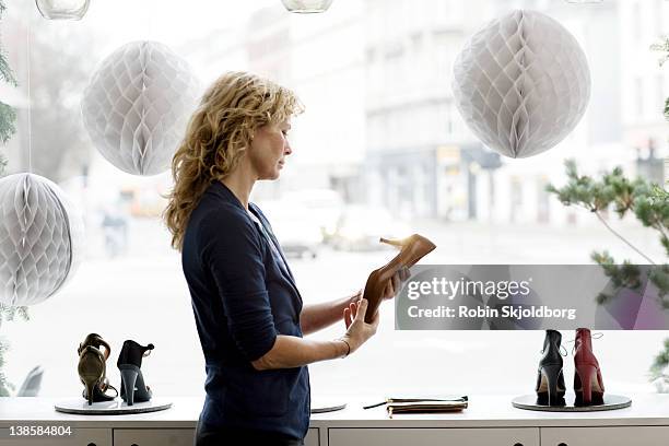 woman standing in shoe store looking at shoes - magasin de chaussures photos et images de collection