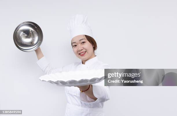 asian female chef wearing a chef's hat and carrying a domed tray and holding a empty plate. advertisement material - frau mit tablett stock-fotos und bilder