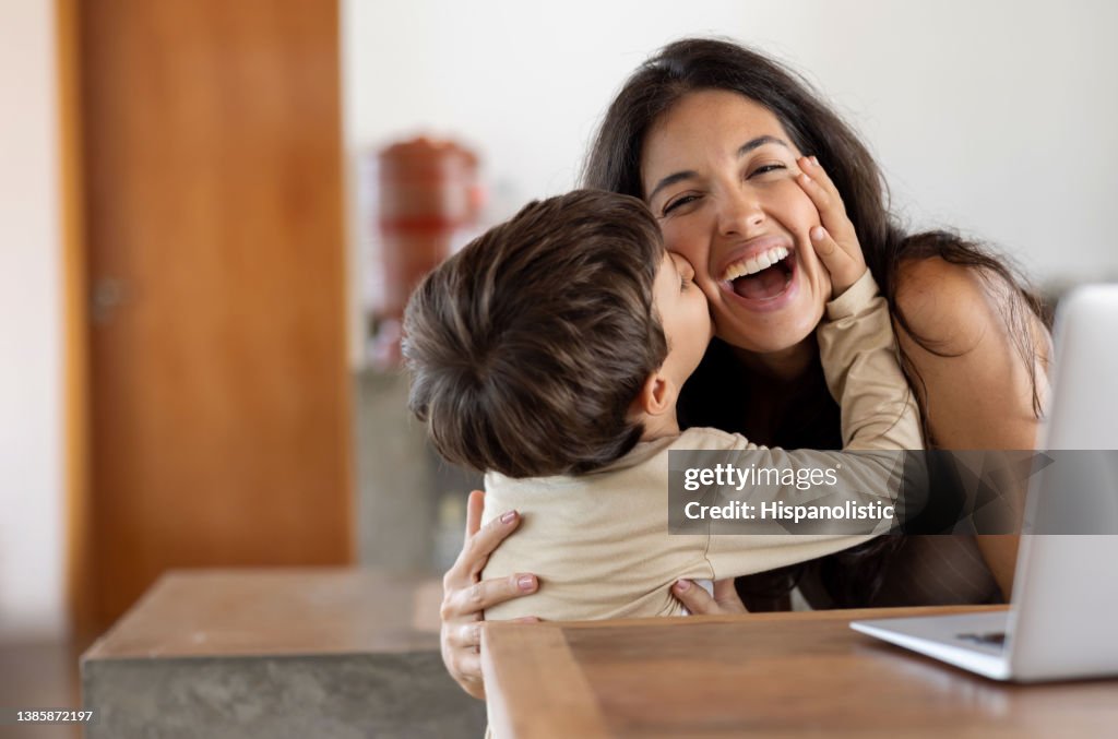 Filho amoroso dando um beijo em sua mãe enquanto ela está trabalhando em casa