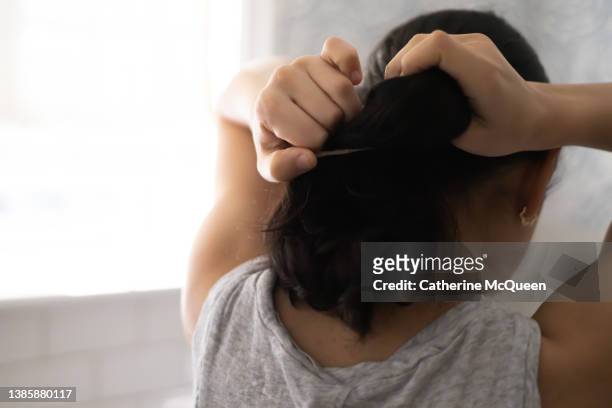 mixed-race female standing in front of bathroom mirror putting hair in ponytail - hair back bildbanksfoton och bilder