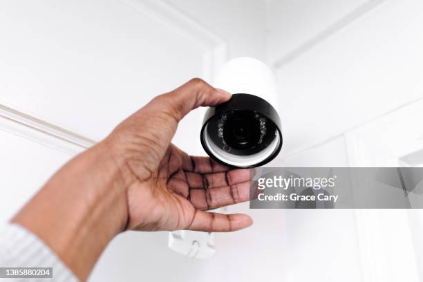 woman adjusts outdoor security camera - camera de surveillance photos et images de collection