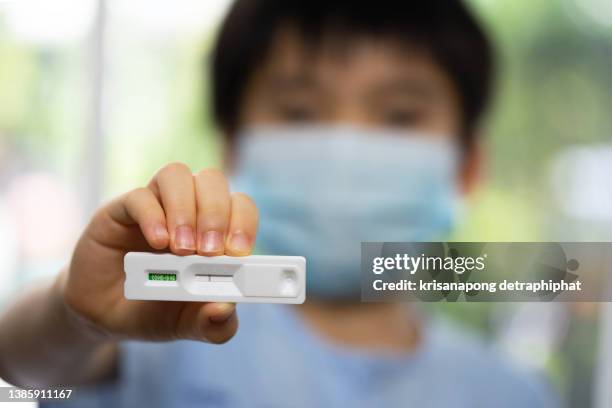 boy holding rapid antigen test kit with positive result during swab covid-19 testing. coronavirus self nasal or home test, lockdown and home isolation concept - flatten the curve icon stock pictures, royalty-free photos & images