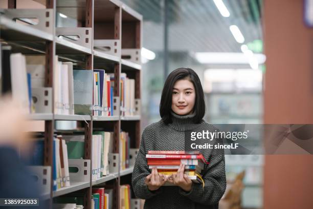 asian female students holding for selection book in library - literature stock pictures, royalty-free photos & images