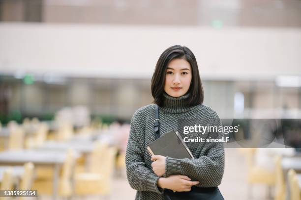 studentesse asiatiche in possesso di selezione libro in biblioteca - asian college student foto e immagini stock