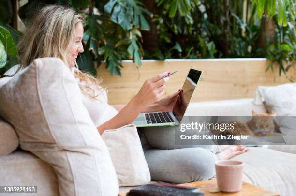 woman sitting on sofa, using laptop and holding credit card - cream colored purse 個照片及圖片檔