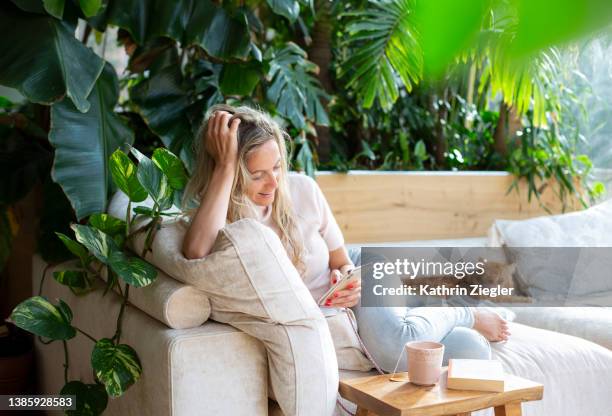 woman relaxing on sofa, text messaging on mobile phone - cat looking up bildbanksfoton och bilder