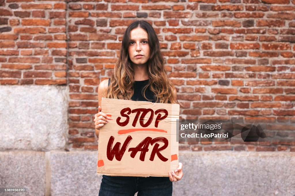 Portrait of a young woman holding a sign against War