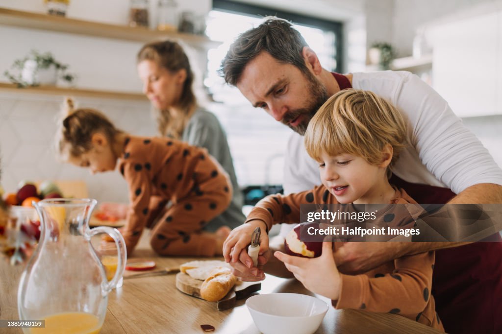 Young family with two little children preparing breakfast together in kitchen.