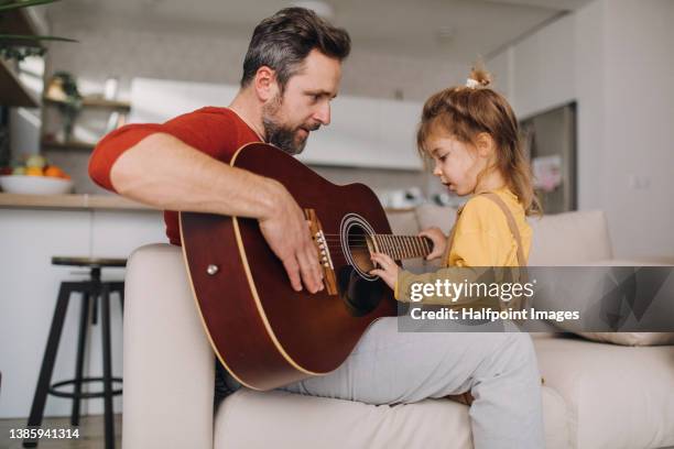 mid adult father learning his little daughter to play guitar at home. - teach muziekinstrument stockfoto's en -beelden