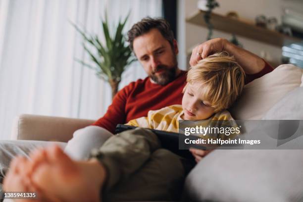 little boy with his father sitting on sofa and using tablet at home. - tablet screen home stock-fotos und bilder