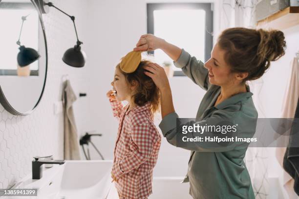 mother with small child indoors in bathroom in the morning at home, brushing teeth and hair. - mom and young daughter stockfoto's en -beelden