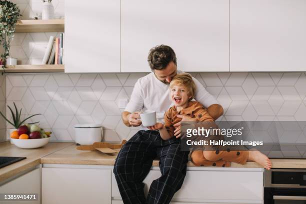 father sitting on kitchen counter with his little son and having morning coffee. - küche familie stock-fotos und bilder