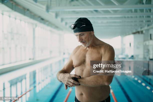 active senior man swimmer setting smart watch before swimming in indoors swimming pool. - man in swimming pool stockfoto's en -beelden