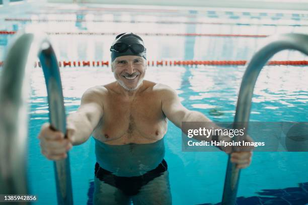 active senior man swimmer holding onto ladder in indoors swimming pool and looking at camera. - portrait schwimmbad stock-fotos und bilder
