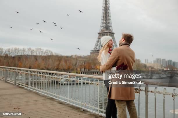 romantic couple hugging each other closely while standing on a bridge at seine river with eiffel tower, paris, in background - couple paris stockfoto's en -beelden