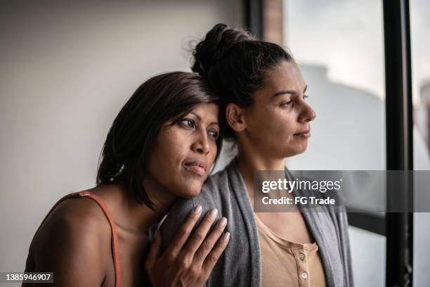 contemplative lesbian couple looking through window at home - sad gay person stock pictures, royalty-free photos & images