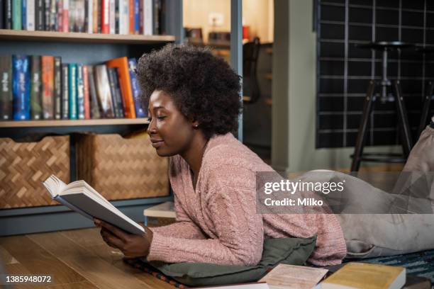 young african-american woman reading a book at home on the floor - authors night stockfoto's en -beelden