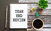 Selective focus of pencil,mobile phone and notebook written with Year End Review on white wooden background