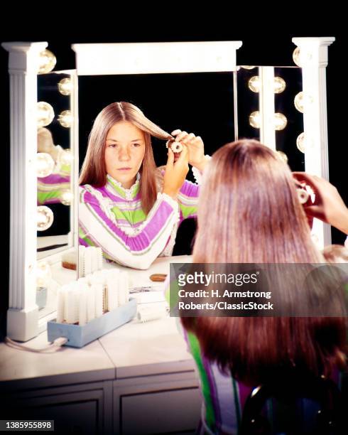 1970s Teen Girl With Long Brown Hair Parted In Middle Sitting In Front Of Vanity Mirror Putting Hot Rollers In Her Hair.