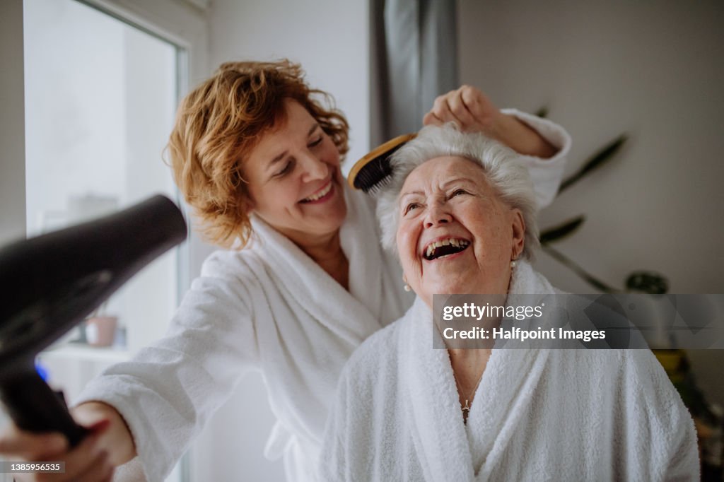 Senior mother with mature daughter in bathrobes having spa day at home together.