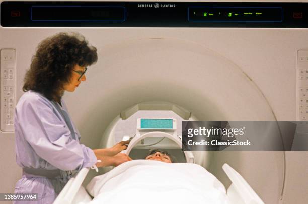1980s Medical Technician With Patient Operating A Nuclear Magnetic Resonance Imaging Mri Scanner.
