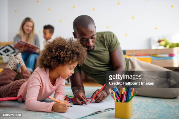 little multiracial girl lying on floor and doing homework with his father at home. - teacher school supplies stock pictures, royalty-free photos & images