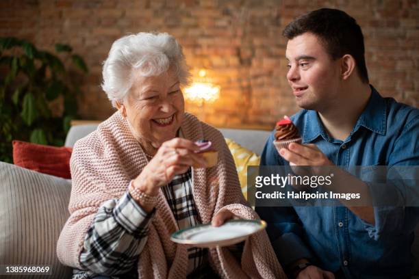 grandmother enjoying cupcakes with her grandson with down syndrome at home. - man eating pie stock pictures, royalty-free photos & images