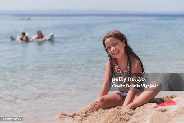 fille heureuse assise dans le sable de la plage et riant - ado en maillot de bain photos et images de collection