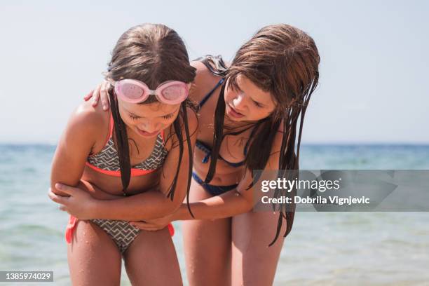 girl having stomach cramps and her sister taking her out of the water - tween girl swimsuit stockfoto's en -beelden