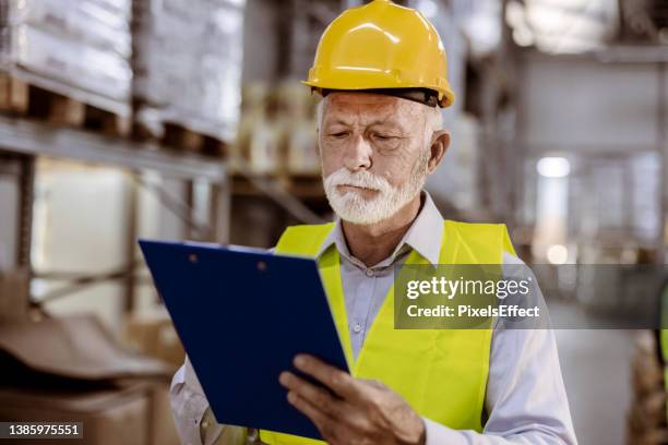 senior male warehouse worker with a clipboard in distribution warehouse - elderly receiving paperwork stock pictures, royalty-free photos & images