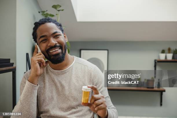 portrait of african american man holding a pill bottle - doctor using phone stock pictures, royalty-free photos & images