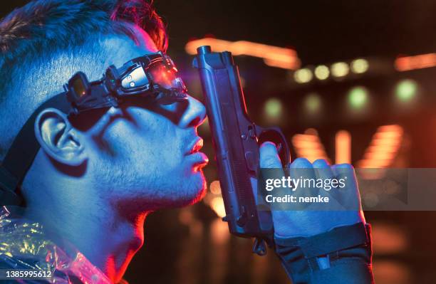 young gangster holding a gun with neon city lights in background at night - street villains stock pictures, royalty-free photos & images