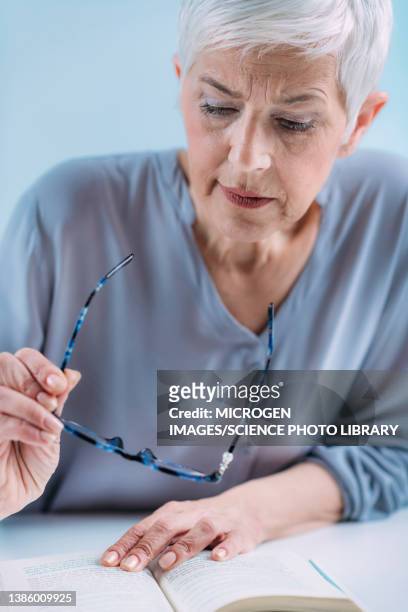 senior woman reading a book whilst holding reading glasses - entrecerrar los ojos fotografías e imágenes de stock