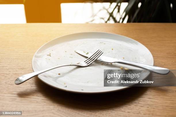 a dirty empty plate, fork and knife on a wooden table. used cutlery, symbolizing the end of lunch or dinner. - bestek stockfoto's en -beelden