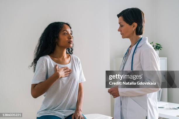 worried mature female doctor carefully listening to complaints of african-american patient - hjärtattack bildbanksfoton och bilder