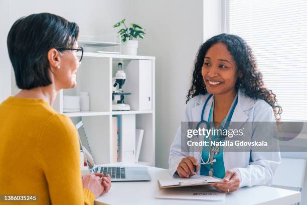 african-american doctor putting down medical complaints on clipboard in clinic office - doctor looking down stock pictures, royalty-free photos & images