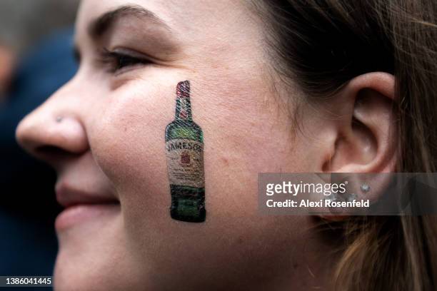 Woman poses with a temporary tattoo of a whiskey bottle on her face at the St. Patrick’s Day parade on March 17, 2022 in New York City. The annual...