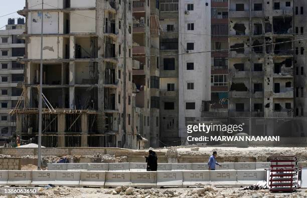 Lebanese women wearing Islamic headscarves walk in front of partially destroyed and empty buildings which are still untouched at Hezbollah's security...