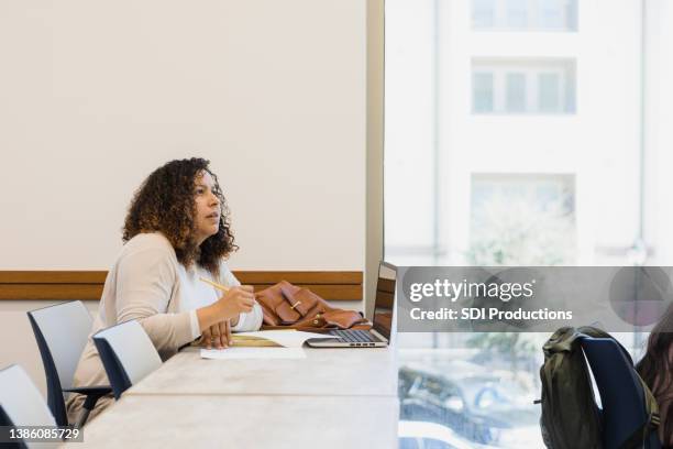 woman with laptop open writes lecture notes by hand - student government stock pictures, royalty-free photos & images